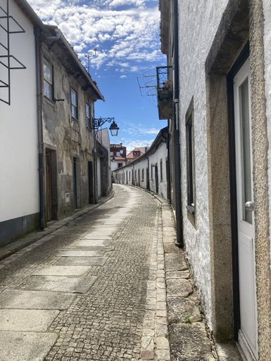 Eine schmale, gepflasterte Gasse mit historischen Gebäuden und einem klaren blauen Himmel im Hintergrund.