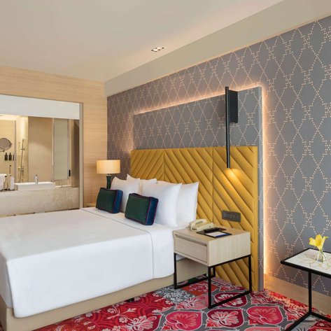 Ein modernes Hotelzimmer mit einem großen Bett, bunten Kissen und einem eleganten Nachttisch mit einer Blume.