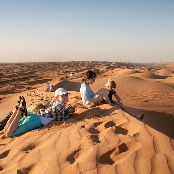Kinder sitzen gemeinsam auf einer Wüstendüne – Oman Familienreise