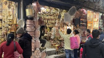 In einer belebten Straße in Kathmandu betrachten Menschen eine Vielzahl von Kupferwaren und Souvenirs in einem Geschäft.