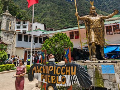Eine goldene Statue eines Inka-Herrschers steht stolz vor den majestätischen Anden, umgeben von einem lebhaften Dorf.