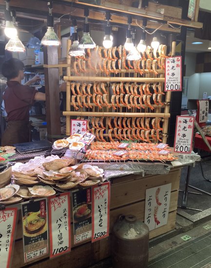 Ein Marktstand in Kyoto bietet eine Vielzahl von gegrillten Garnelen und Meeresfrüchten, umgeben von warmem Licht.