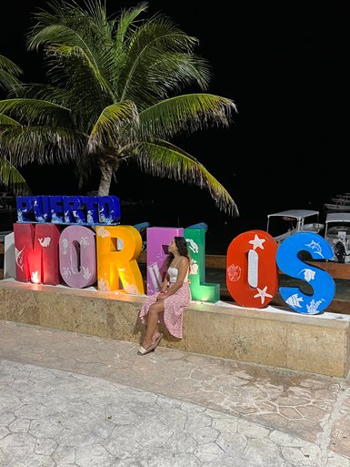 Mädchen sitzt vor dem farbenfrohen Puerto-Morelos-Schriftzug – Mexiko Familienreise