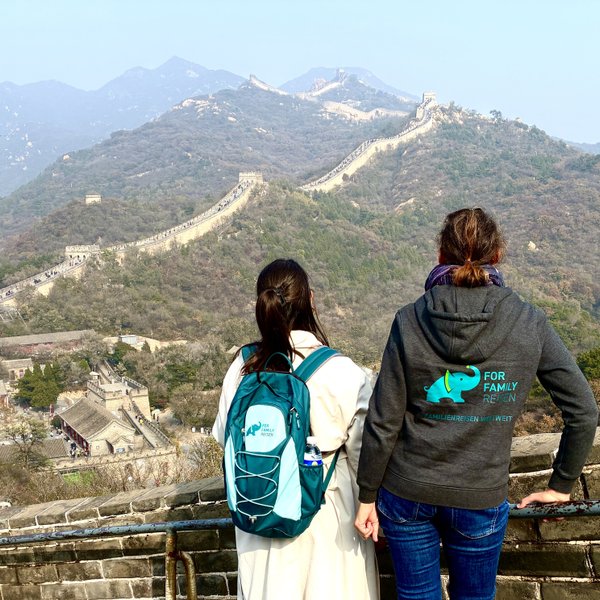Zwei Frauen stehen auf der Chinesischen Mauer und blicken auf die beeindruckende Landschaft der Berge und Wälder.