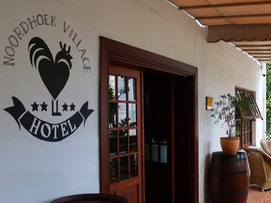 Der Eingangsbereich des Noordhoek Village Hotels zeigt eine einladende Atmosphäre mit Pflanzen und einem gemütlichen Sessel.
