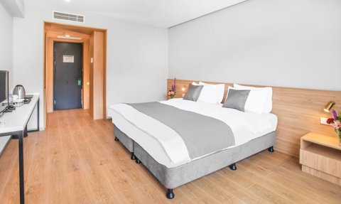 Ein modernes Hotelzimmer mit einem großen Doppelbett, eleganten Kissen und einem Holzregal mit frischen Blumen.
