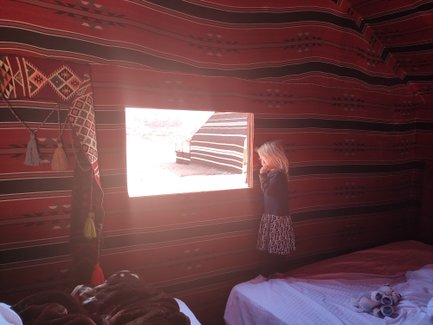 Ein kleines Mädchen steht am Fenster eines Zeltzimmers und schaut nach draußen in die Wüste von Wadi Rum.