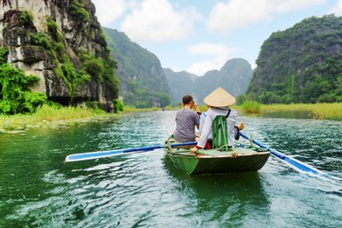 Zwei Personen sitzen in einem Boot und genießen die ruhige Landschaft mit hohen, bewaldeten Klippen im Hintergrund.