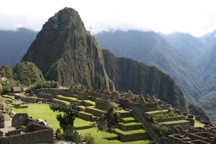 Die beeindruckenden Ruinen von Machu Picchu liegen auf einer grünen Terrasse, umgeben von majestätischen Bergen und Wolken.
