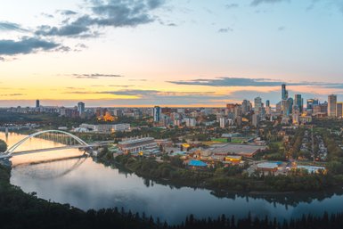 Die Skyline von Edmonton bei Sonnenuntergang, mit reflektierenden Wolken über dem ruhigen Fluss und der Stadt im Hintergrund.