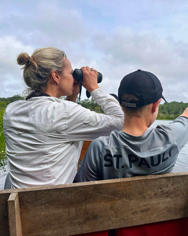 Eine Frau mit blonden Haaren beobachtet mit einem Fernglas die Umgebung, während ein Junge auf das Wasser zeigt.