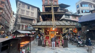 Ein geschäftiger Platz in Kathmandu mit einem prächtigen Tempel, umgeben von historischen Gebäuden und Menschen, die beten.