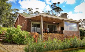 Ein charmantes, gemauertes Ferienhaus mit einem einladenden Garten und einer Veranda, umgeben von üppiger Natur.
