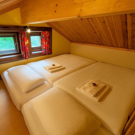 Ein gemütliches Schlafzimmer in einer Hütte mit zwei Betten, frischen Handtüchern und bunten Vorhängen an den Fenstern.