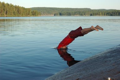 Ein Junge springt kopfüber in einen ruhigen See, während die Sonne auf die Wasseroberfläche scheint.