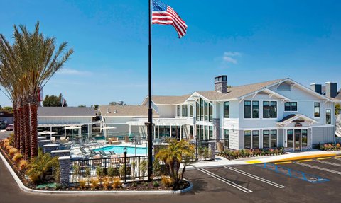 Ein modernes Hotelgebäude mit einem einladenden Poolbereich, umgeben von Palmen und Sonnenschirmen, unter strahlend blauem Himmel.