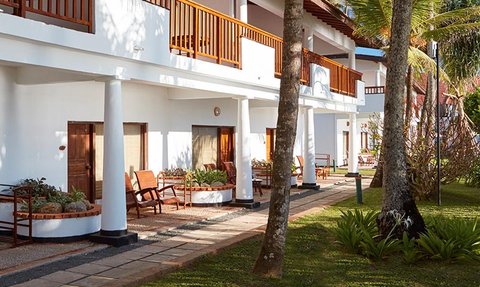 Die Ansicht zeigt ein elegantes Resort mit weißen Wänden, Holzveranden und einem gepflegten Garten unter strahlend blauem Himmel.