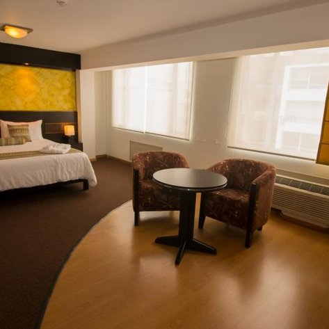 Ein modernes Hotelzimmer mit einem großen Bett, zwei gemütlichen Sesseln und einem kleinen Tisch, umgeben von natürlichem Licht.