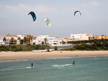 Drei Kitesurfer gleiten über das Wasser, während bunte Kites über ihnen in einem klaren Himmel schweben.
