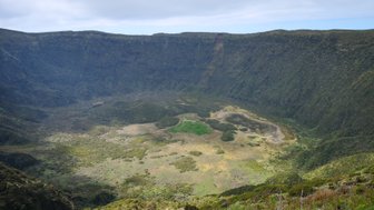 Ein beeindruckender Vulkankrater mit üppiger Vegetation und einem ruhigen, grünen See im Inneren, umgeben von steilen Hängen.