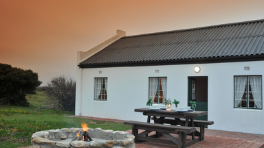 Ein gemütliches Haus mit einem einladenden Außenbereich, umgeben von sanften Hügeln und einem warmen, orangefarbenen Himmel.