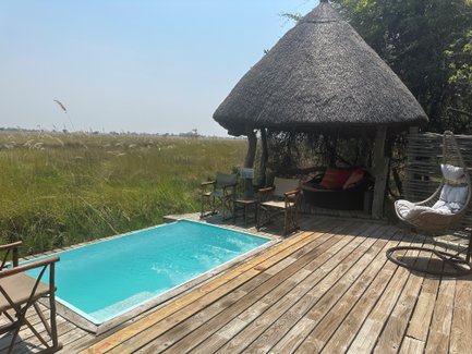 Ein einladender Pool in einem Camp, umgeben von üppigem Gras und einem schattigen Pavillon mit gemütlichen Sitzgelegenheiten.
