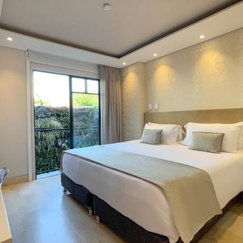 Ein modernes Hotelzimmer mit einem großen Doppelbett, sanften Farben und einem Fenster, das auf eine grüne Landschaft blickt.