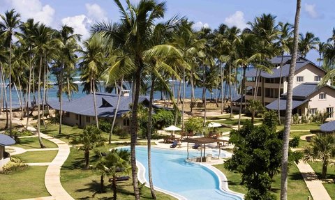Ein tropisches Resort mit einem glitzernden Pool, umgeben von Palmen und Blick auf das Meer, ideal für Entspannung.