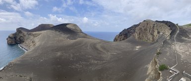Eine beeindruckende Küstenlandschaft mit schwarzen Sanddünen, die sanft ins blaue Wasser übergehen, unter einem bewölkten Himmel.