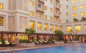 Ein eleganter Hotelpool mit Liegen und Palmen, umgeben von einem modernen Gebäude mit kunstvollen Fenstern.
