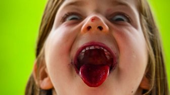 Ein fröhliches Kind zeigt seine Zunge, die mit roter Farbe bedeckt ist, und hat einen ausgelassenen Gesichtsausdruck.