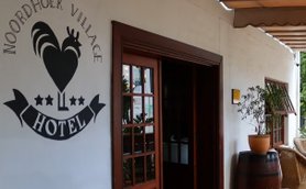 Der Eingangsbereich des Noordhoek Village Hotels zeigt eine einladende Atmosphäre mit Pflanzen und einem gemütlichen Sessel.