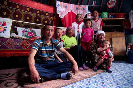 Eine Nomadenfamilie sitzt in ihrem Zelt, umgeben von bunten Kissen und traditionellen Teppichen, während sie in die Kamera lächeln.