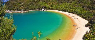 Eine malerische Bucht mit klarem, türkisfarbenem Wasser und feinem Sandstrand, umgeben von üppigem Grün.
