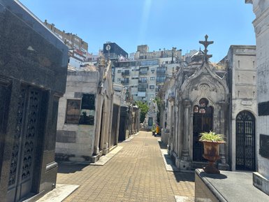 Ein sonniger Tag im Friedhof von Buenos Aires, mit eleganten Grabstätten und modernen Gebäuden im Hintergrund.