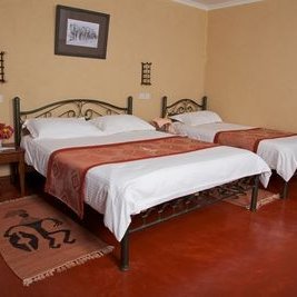 Ein gemütliches Zimmer mit zwei Einzelbetten, dekoriert mit roten Überwürfen und einem stilvollen Teppich auf dem Boden.