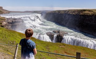 Ein Junge steht am Rand einer Klippe und beobachtet den beeindruckenden Gullfoss-Wasserfall in Island.