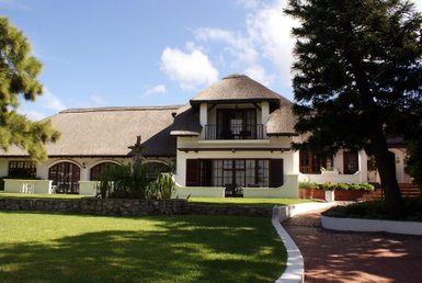Ein elegantes, strohgedecktes Haus mit einem gepflegten Garten und einer Steinmauer, umgeben von Bäumen und blauem Himmel.