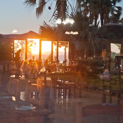 Ein gemütliches Restaurant mit Tischen und Stühlen, während die Sonne hinter den Palmen untergeht.