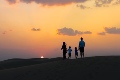 Familie genießt den Sonnenuntergang über den Dünen im Thousand Nights Camp – Oman mit Kindern