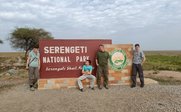 Eine Gruppe von vier Personen posiert fröhlich vor dem Eingangsschild des Serengeti-Nationalparks in Tansania.