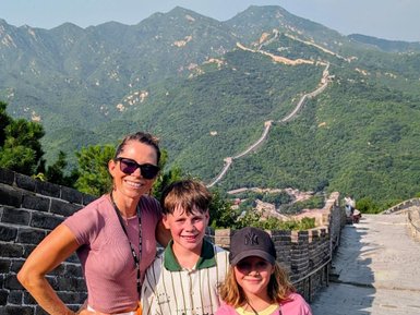 Eine fröhliche Familie posiert auf der Chinesischen Mauer, umgeben von grünen Bergen und strahlendem Sonnenschein.
