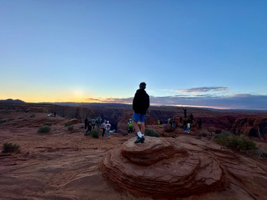 Ein junger Mann steht auf einem Felsen und blickt auf die beeindruckende Landschaft von Horseshoe Bend bei Sonnenuntergang.