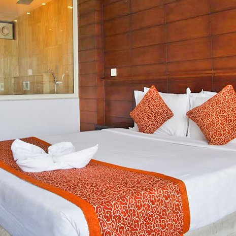 Ein modernes Hotelzimmer mit einem großen Bett, dekoriert mit orangefarbenen Kissen und einer eleganten Bettdecke.