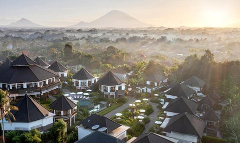 Eine atemberaubende Aussicht auf ein Resort mit traditionellen Dächern, umgeben von üppiger Natur und Bergen im Hintergrund.
