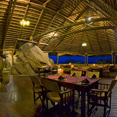 Ein stilvolles Restaurant mit einem hohen Strohdach, umgeben von großen Felsen und sanfter Beleuchtung für eine gemütliche Atmosphäre.