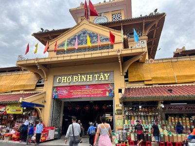 Der Eingang zum Chợ Bình Tây ist mit bunten Fahnen geschmückt, während Menschen geschäftig um die Stände herumgehen.