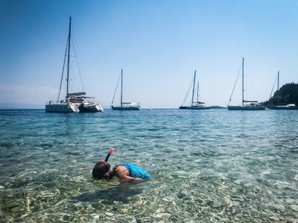 Ein Kind mit Schnorchel taucht in das klare Wasser, umgeben von mehreren Segelbooten im Hintergrund.