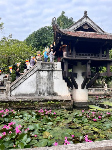 Eine Gruppe von Menschen erkundet die beeindruckende Ein-Säulen-Pagode in Hanoi, umgeben von blühenden Seerosen.