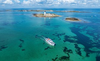 Ein Boot fährt durch das klare, türkisfarbene Wasser, umgeben von kleinen Inseln und einem strahlend blauen Himmel.